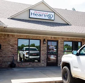 Natural Hearing Centers clinic building exterior with signage and parking in front
