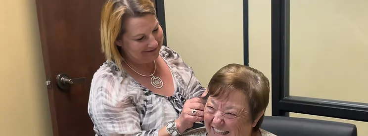 Provider adjusting a hearing aid on a smiling patient during an appointment
