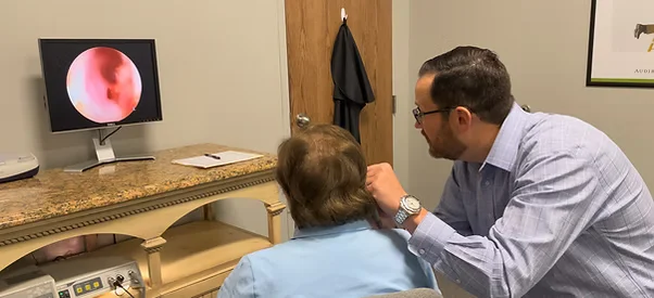 Hearing specialist examining a patient’s ear while viewing ear canal image on a monitor